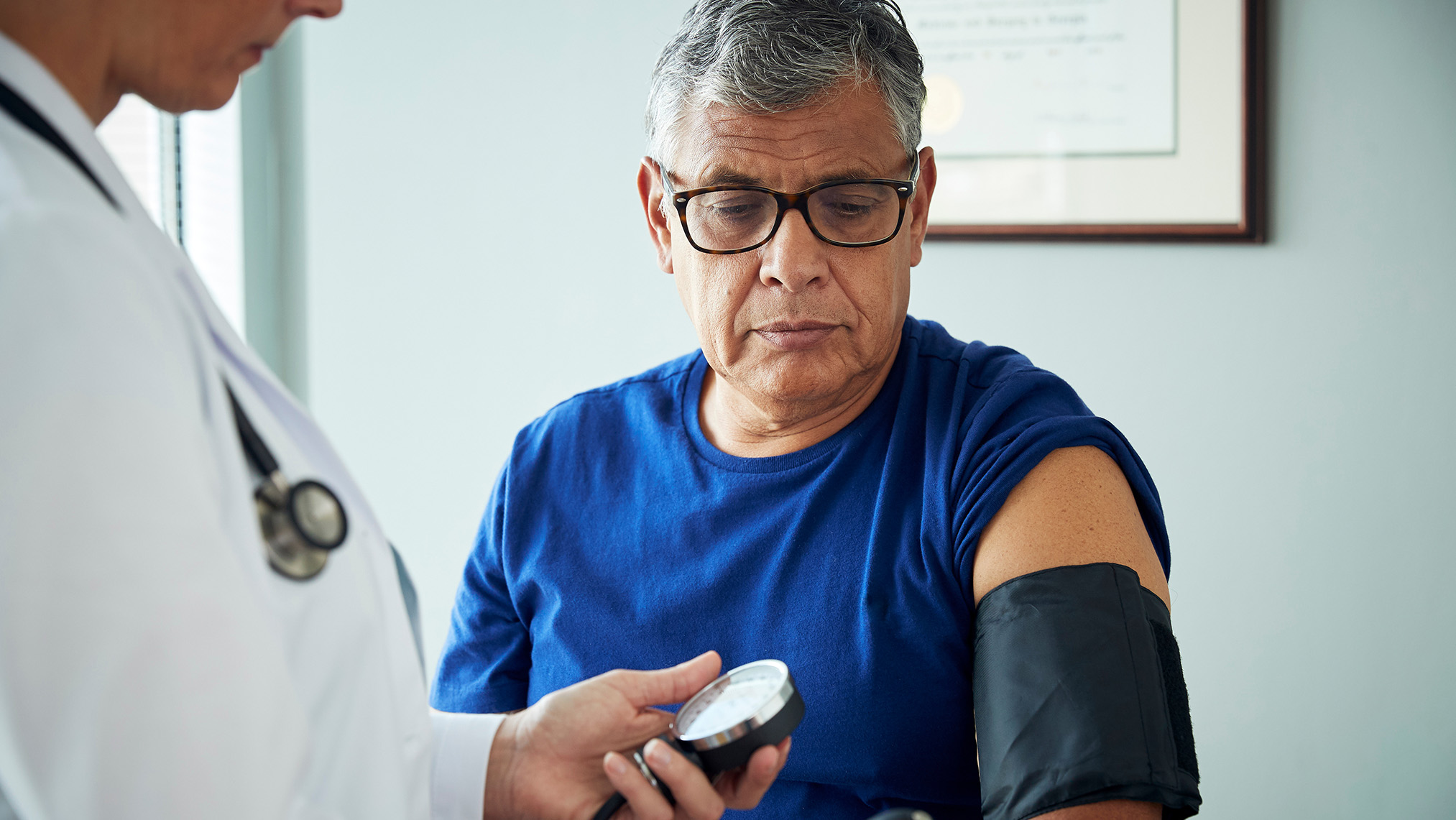 A man is seated while a doctor measures his blood pressure.